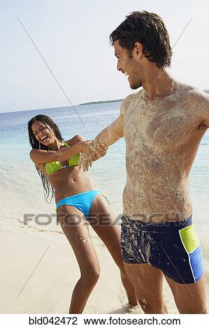 Stock Image - South American woman pulling boyfriend at beach. Fotosearch