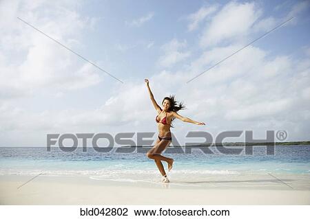 Stock Image - South American woman running on beach. Fotosearch