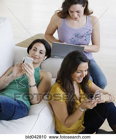 Stock Image - Three young women using wireless devices. Fotosearch