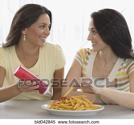 Stock Photography - Two young women eating french fries. Fotosearch