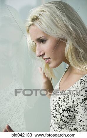 Stock Image - Young woman looking out window. Fotosearch
