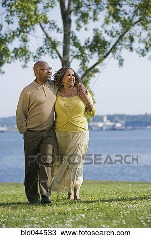 Stock Image - African American couple waking next to water. Fotosearch