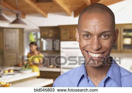 Stock Image - African man smiling with wife in background. Fotosearch