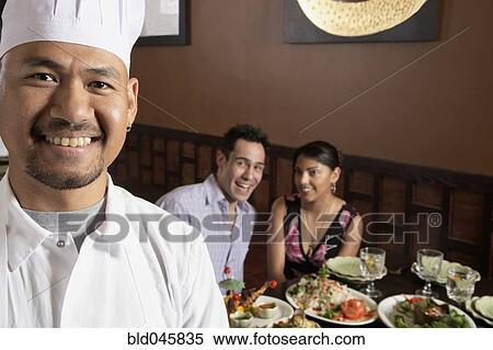 Stock Photography - Asian male chef with diners in background. Fotosearch
