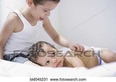 Stock Image - Hispanic baby laying head on brother’s leg. Fotosearch