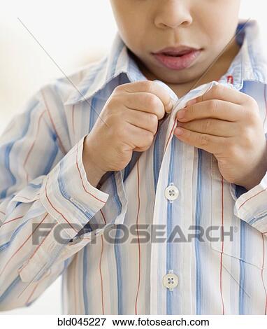 Stock Photo - Hispanic boy buttoning shirt. Fotosearch