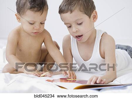 Picture - Hispanic boy reading to baby brother. Fotosearch