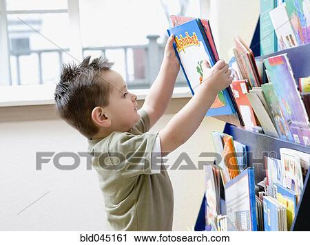 Stock Image - Hispanic boy taking book from rack. Fotosearch