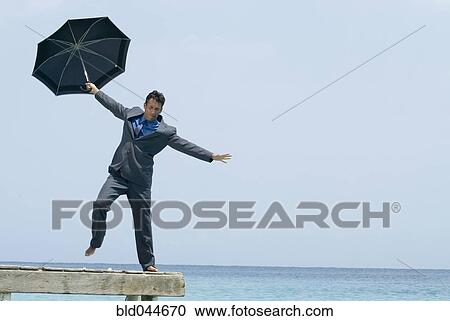 Stock Image - Hispanic businessman holding umbrella on dock. Fotosearch