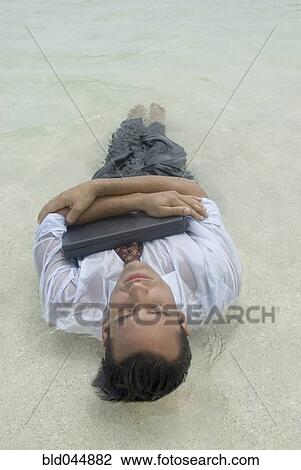 Stock Image - Hispanic businessman hugging laptop in water. Fotosearch