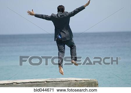 Stock Image - Hispanic businessman jumping off dock. Fotosearch