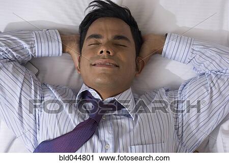 Stock Image - Hispanic businessman laying on bed. Fotosearch