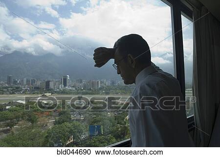 Stock Image - Hispanic businessman looking out window. Fotosearch