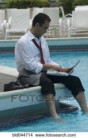 Picture - Hispanic businessman using laptop next to swimming pool. Fotosearch