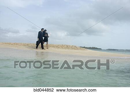 Stock Image - Hispanic businesspeople walking on beach. Fotosearch