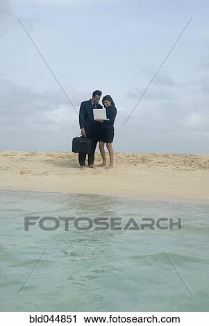 Stock Image - Hispanic businesspeople with laptop at beach. Fotosearch