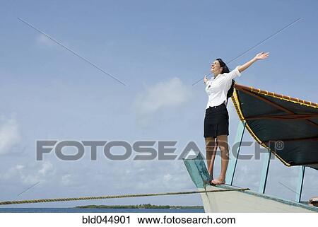 Stock Image - Hispanic businesswoman on boat with arms raised. Fotosearch