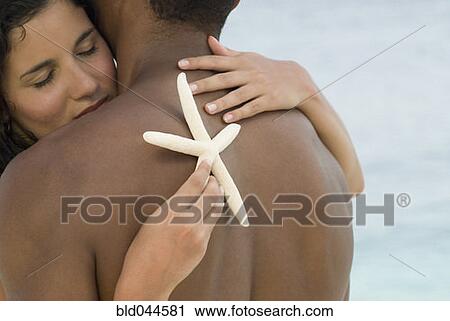 Stock Image - Hispanic couple hugging with starfish. Fotosearch