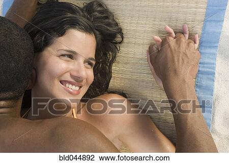 Stock Image - Hispanic couple laying on beach mat. Fotosearch
