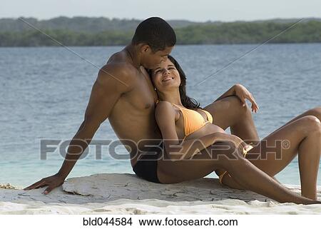 Picture - Hispanic couple sitting on beach. Fotosearch