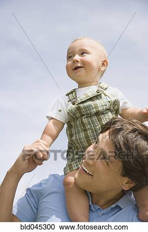 Stock Image - Hispanic father holding baby on shoulders. Fotosearch