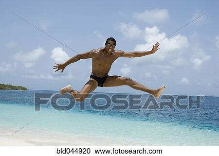 Stock Image - Hispanic man jumping at beach. Fotosearch