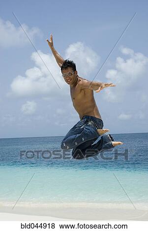 Stock Photo - Hispanic man jumping at beach. Fotosearch