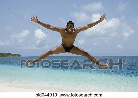 Stock Photo - Hispanic man jumping at beach. Fotosearch