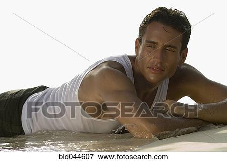 Stock Photo - Hispanic man laying in surf at beach. Fotosearch