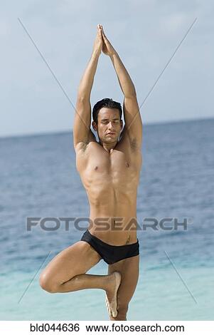Stock Photograph - Hispanic man practicing yoga at beach. Fotosearch