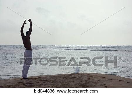 Stock Photograph - Hispanic man practicing yoga at beach. Fotosearch