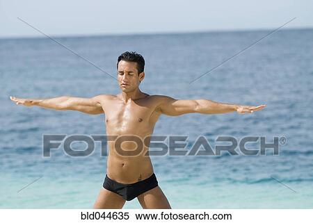 Stock Photography - Hispanic man practicing yoga at beach. Fotosearch