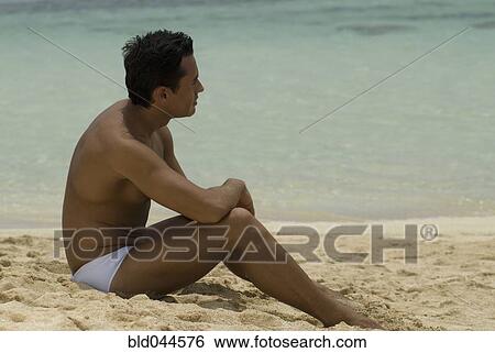 Stock Photograph - Hispanic man sitting on beach. Fotosearch