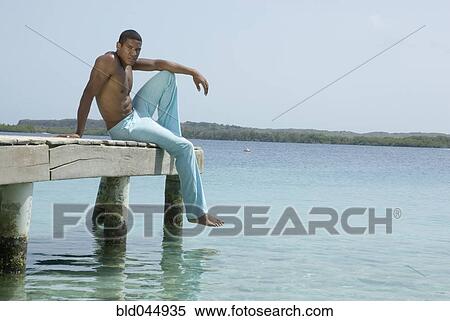 Stock Photography - Hispanic man sitting on dock. Fotosearch