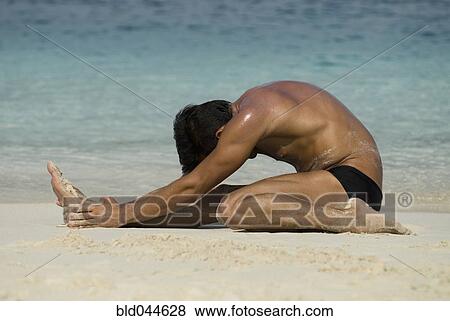 Stock Photo - Hispanic man stretching on beach. Fotosearch