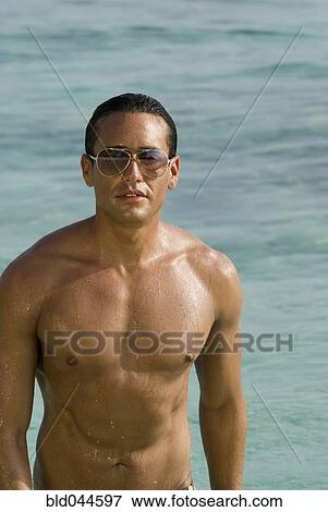 Stock Photo - Hispanic man wearing sunglasses in water. Fotosearch