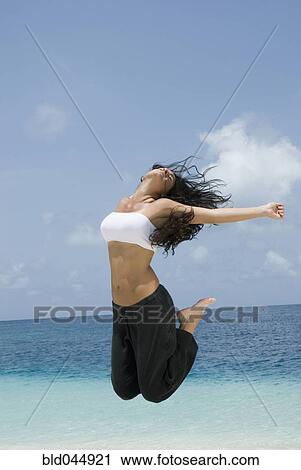 Stock Image - Hispanic woman jumping at beach. Fotosearch