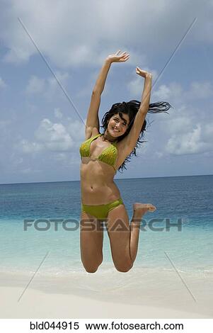 Stock Photography - Hispanic woman jumping at beach. Fotosearch