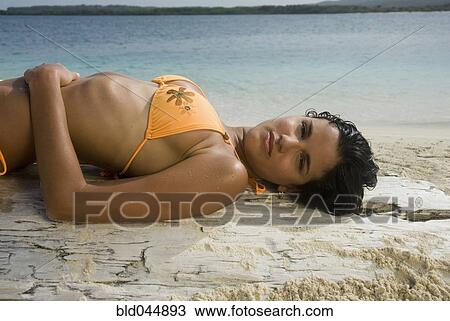 Stock Image - Hispanic woman laying on driftwood log. Fotosearch