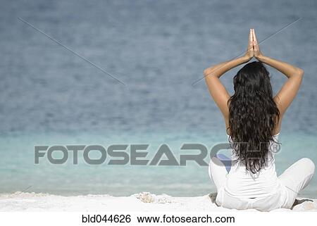 Stock Photograph - Hispanic woman practicing yoga at beach. Fotosearch