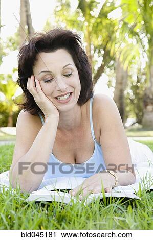 Stock Image - Hispanic woman reading in grass. Fotosearch