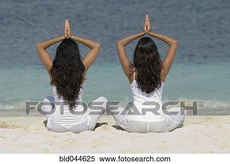 Stock Photography - Hispanic women practicing yoga at beach. Fotosearch