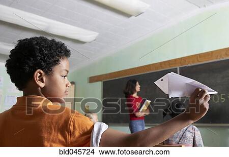 Picture - Mixed Race boy throwing paper airplane in class. Fotosearch