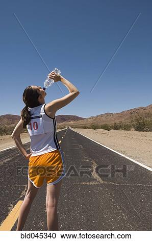 Stock Image - Mixed Race female runner drinking water. Fotosearch