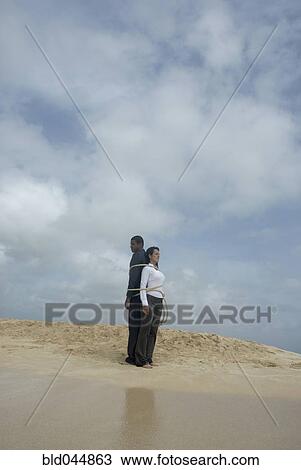 Stock Image - Multi-ethnic businesspeople tied together at beach. Fotosearch
