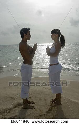 Stock Image - Multi-ethnic couple practicing yoga on beach. Fotosearch