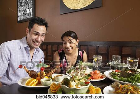 Stock Image - Multi-ethnic couple with table full of food. Fotosearch