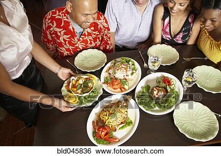 Multi-ethnic friends looking at table full of food View Large Photo Image Stock Photograph - Multi-ethnic friends looking at table full of food. Fotosearch