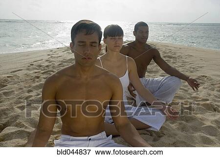 Stock Photo - Multi-ethnic friends meditating on beach. Fotosearch
