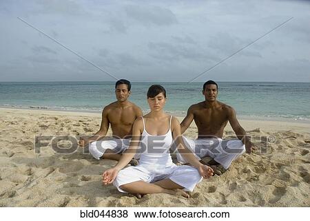 Stock Photo - Multi-ethnic friends meditating on beach. Fotosearch